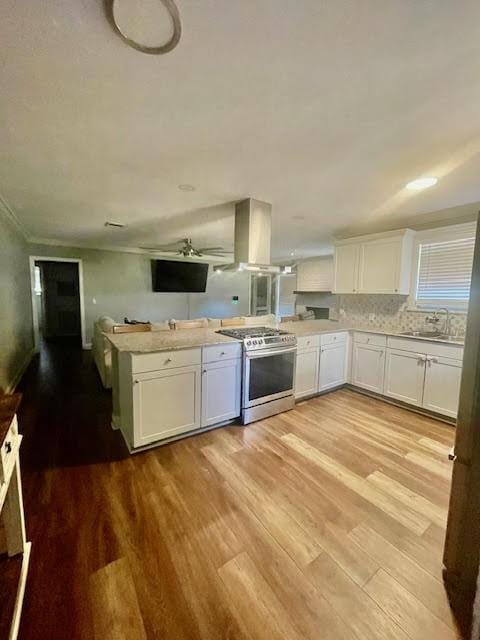 kitchen with white cabinets, island range hood, kitchen peninsula, and stainless steel stove