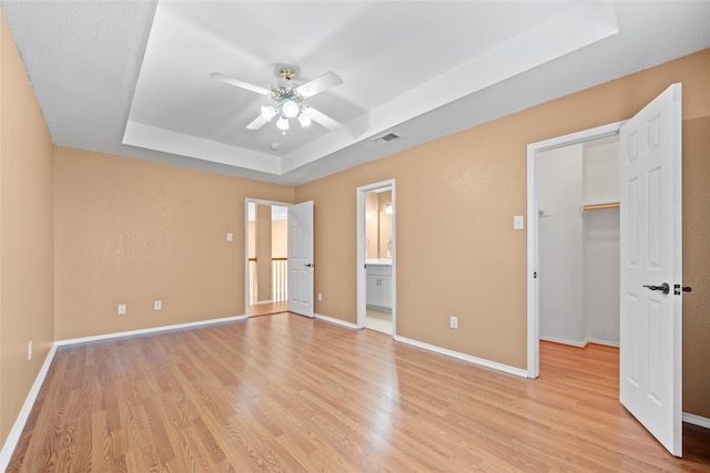 unfurnished bedroom featuring a walk in closet, a tray ceiling, light hardwood / wood-style flooring, and ceiling fan