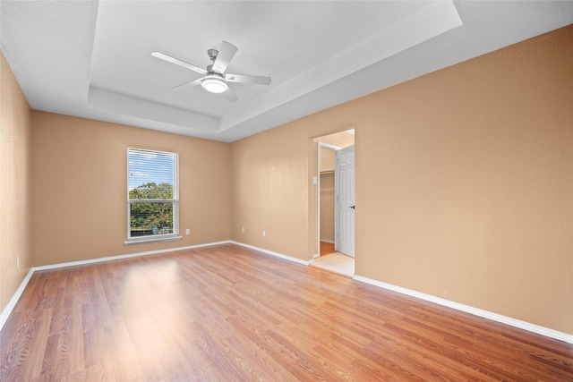 empty room with ceiling fan, light wood-type flooring, and a tray ceiling