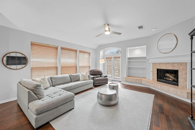 living room with ceiling fan, built in features, a fireplace, and dark wood-type flooring