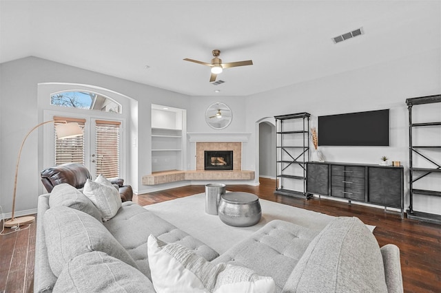 living room with built in features, dark wood-type flooring, and a tiled fireplace