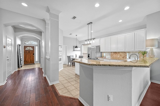 kitchen featuring kitchen peninsula, backsplash, stainless steel appliances, decorative light fixtures, and white cabinetry