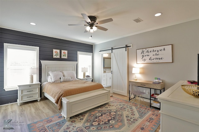 bedroom featuring ensuite bathroom, crown molding, light hardwood / wood-style flooring, ceiling fan, and a barn door