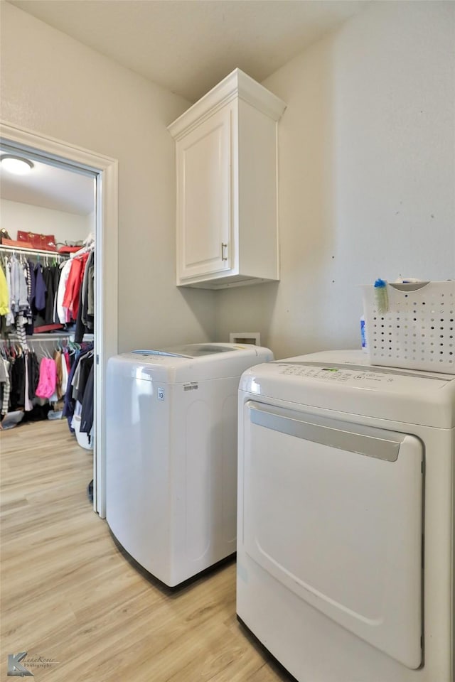 laundry area with washer and clothes dryer, cabinets, and light wood-type flooring