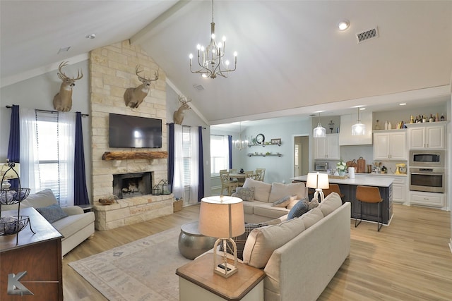 living room featuring an inviting chandelier, a stone fireplace, and light hardwood / wood-style flooring