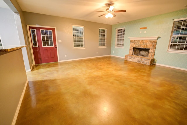 unfurnished living room with concrete floors, a stone fireplace, and ceiling fan