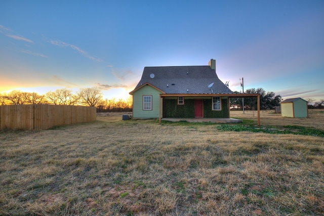 back house at dusk with a patio, a storage shed, and a lawn