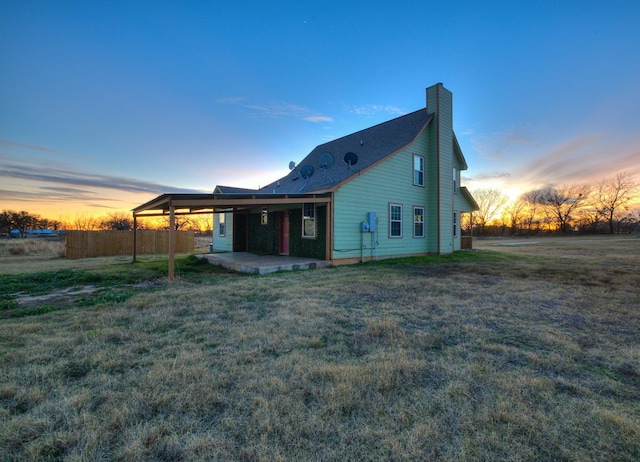 back house at dusk featuring a yard and a patio