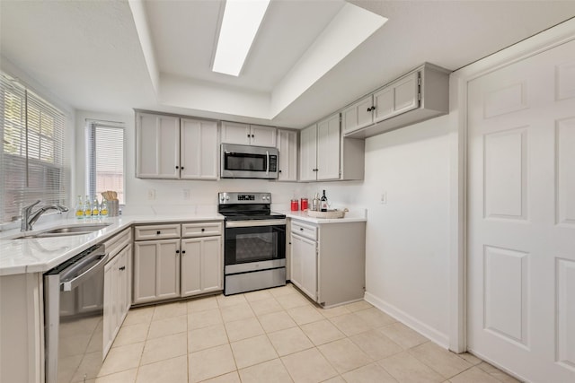 kitchen featuring light tile patterned flooring, stainless steel appliances, a tray ceiling, and sink