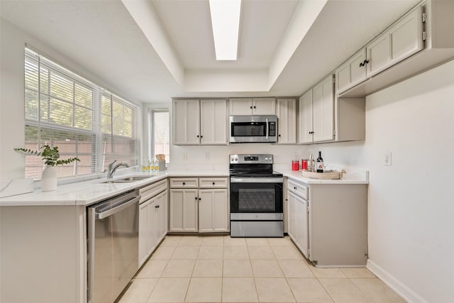 kitchen featuring sink, light tile patterned floors, a tray ceiling, white cabinets, and appliances with stainless steel finishes