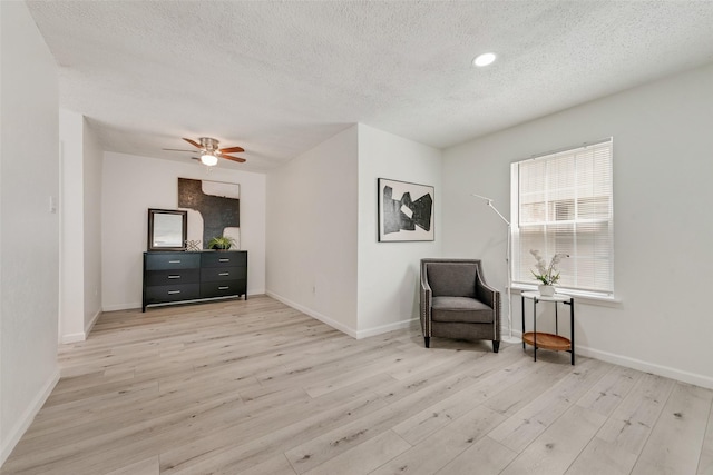 living area with ceiling fan, a textured ceiling, and light hardwood / wood-style flooring