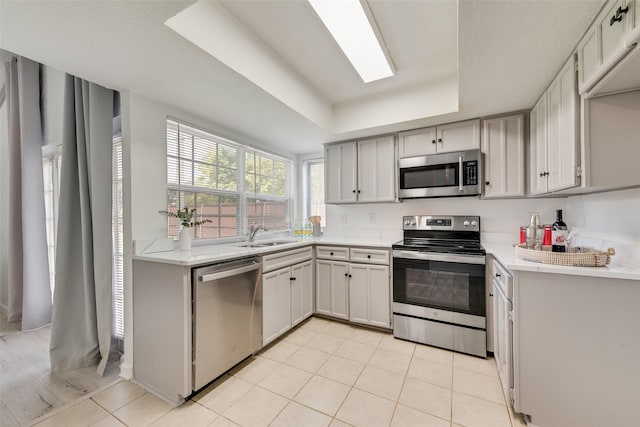 kitchen with light tile patterned flooring, sink, a skylight, appliances with stainless steel finishes, and a raised ceiling