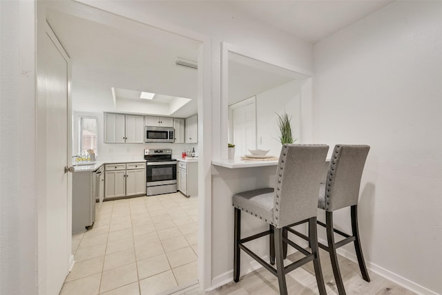 kitchen featuring appliances with stainless steel finishes, a kitchen breakfast bar, a skylight, a raised ceiling, and light tile patterned floors