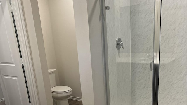 bathroom featuring a shower with door and toilet