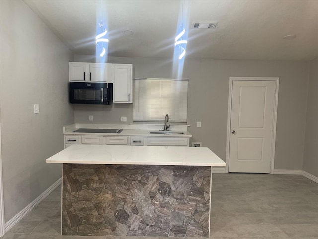 kitchen with sink, a kitchen island, light stone counters, white cabinets, and black appliances