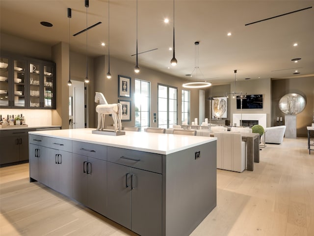 kitchen with gray cabinetry, decorative light fixtures, a large island with sink, and light hardwood / wood-style flooring