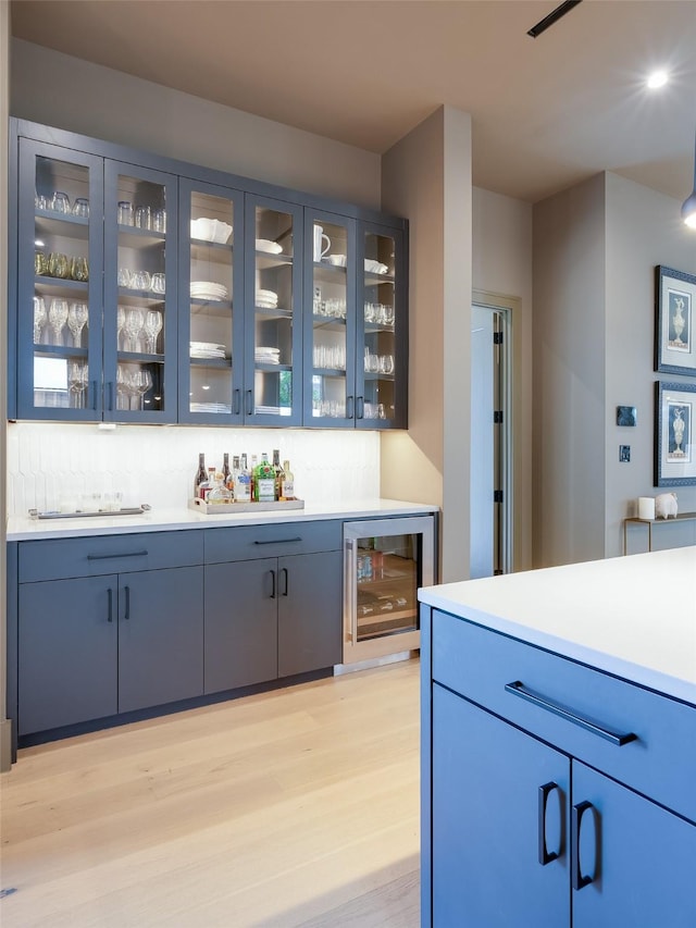 bar featuring light hardwood / wood-style floors, blue cabinets, wine cooler, and tasteful backsplash