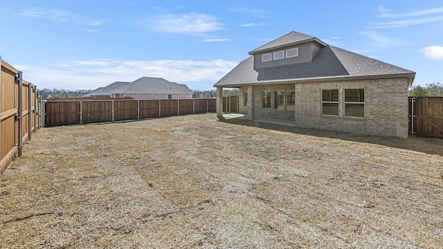 rear view of property with a fenced backyard, brick siding, and roof with shingles