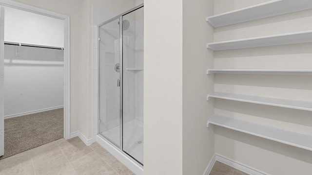 full bath with a walk in closet, baseboards, a stall shower, and tile patterned flooring