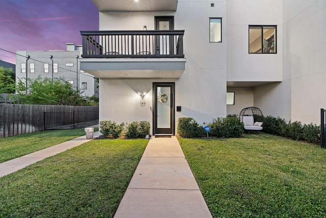 exterior entry at dusk featuring a balcony and a lawn