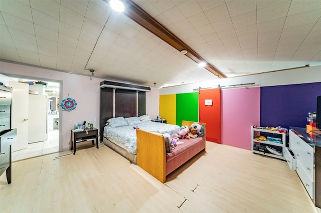 bedroom with beam ceiling, a barn door, light hardwood / wood-style flooring, and white refrigerator