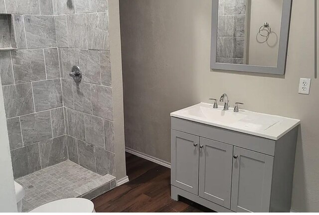 bathroom featuring a tile shower, vanity, wood-type flooring, and toilet