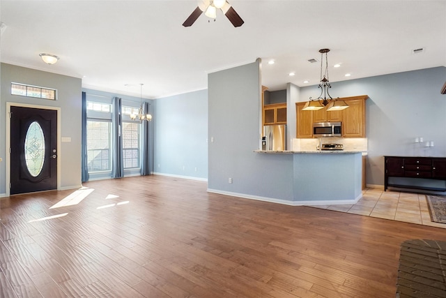 kitchen featuring appliances with stainless steel finishes, light hardwood / wood-style floors, light stone countertops, kitchen peninsula, and ceiling fan with notable chandelier