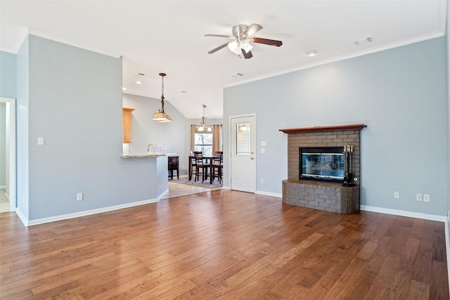 unfurnished living room featuring lofted ceiling, light wood-type flooring, ceiling fan, ornamental molding, and a brick fireplace