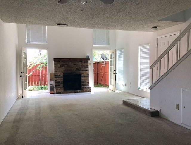 unfurnished living room featuring ceiling fan, light colored carpet, a textured ceiling, and a brick fireplace