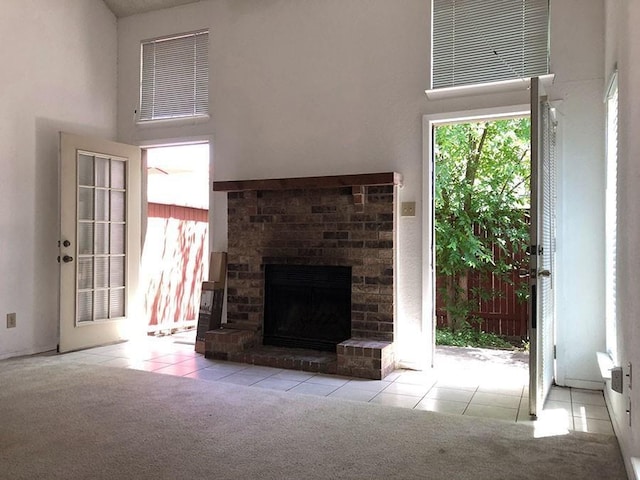 unfurnished living room featuring light carpet, a towering ceiling, and a brick fireplace