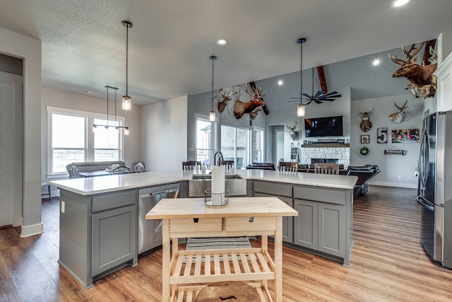 kitchen featuring hanging light fixtures, gray cabinets, a fireplace, a center island with sink, and appliances with stainless steel finishes