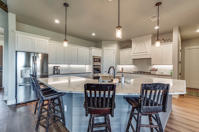 kitchen with a spacious island, custom range hood, decorative light fixtures, white cabinetry, and stainless steel appliances