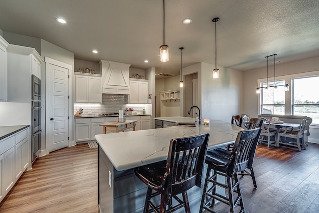 kitchen with white cabinetry, pendant lighting, a spacious island, and custom range hood