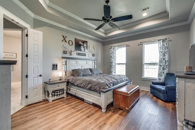 bedroom featuring ornamental molding, a textured ceiling, a raised ceiling, ceiling fan, and wood-type flooring