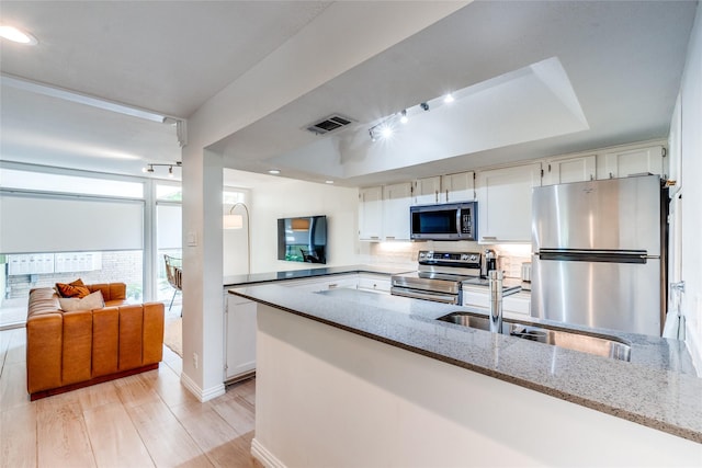 kitchen with appliances with stainless steel finishes, white cabinetry, sink, light stone counters, and kitchen peninsula