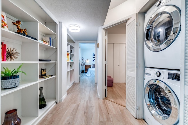 laundry area featuring stacked washer and clothes dryer, a textured ceiling, and light hardwood / wood-style floors