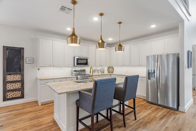 kitchen featuring a center island with sink, light stone counters, white cabinetry, and stainless steel appliances