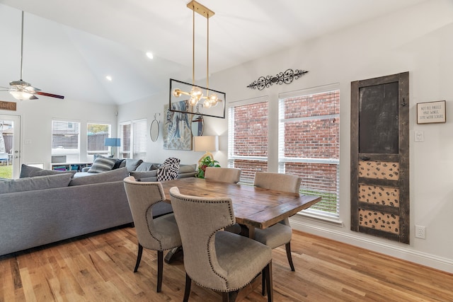 dining area with ceiling fan with notable chandelier, light hardwood / wood-style floors, and high vaulted ceiling