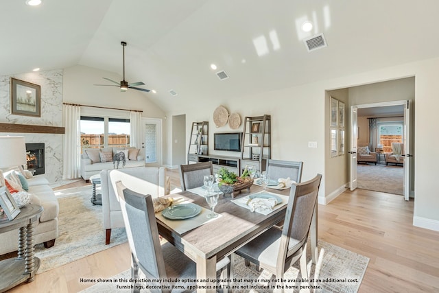 dining room with ceiling fan, a fireplace, lofted ceiling, and light hardwood / wood-style flooring