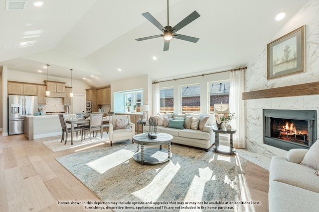 living room with ceiling fan, light hardwood / wood-style flooring, a premium fireplace, and vaulted ceiling