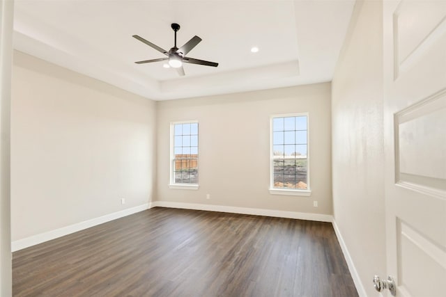 spare room with a tray ceiling, ceiling fan, and dark wood-type flooring