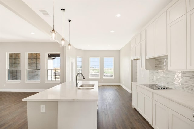 kitchen with black electric cooktop, sink, light stone counters, and a center island with sink