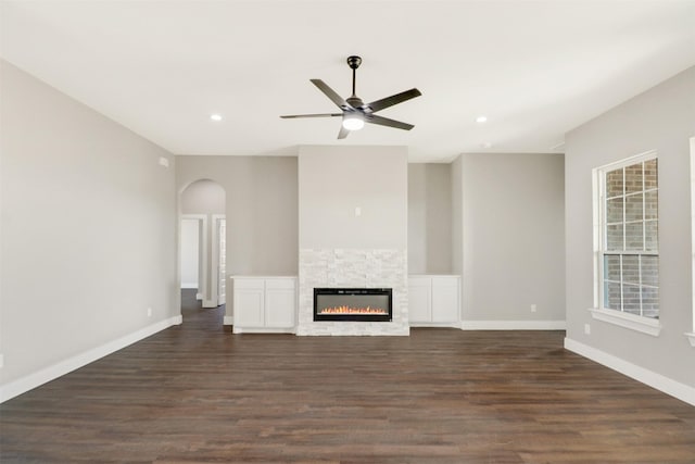 unfurnished living room with ceiling fan, a fireplace, and dark wood-type flooring