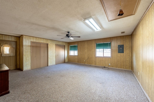 spare room featuring a textured ceiling, light colored carpet, ceiling fan, wooden walls, and electric panel