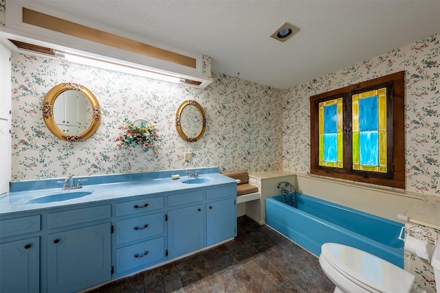 bathroom with a tub to relax in, vanity, a textured ceiling, and toilet