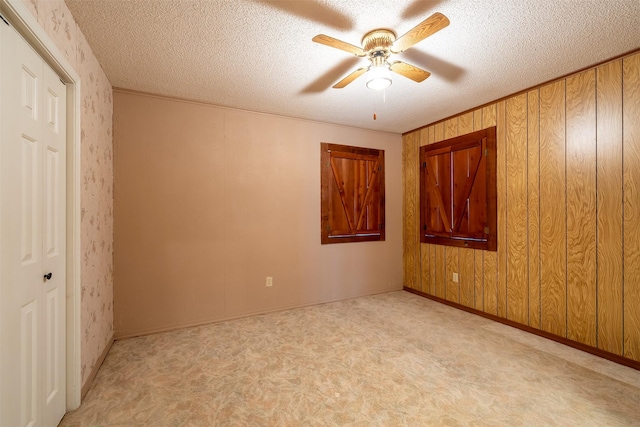 unfurnished bedroom featuring ceiling fan, wooden walls, light colored carpet, and a textured ceiling