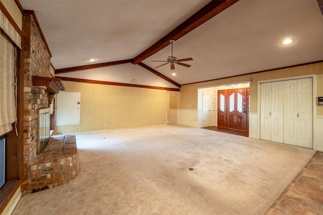 unfurnished living room with lofted ceiling with beams, ceiling fan, a textured ceiling, a fireplace, and carpet floors