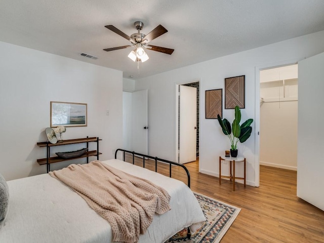 bedroom featuring ceiling fan, light wood-type flooring, a spacious closet, and a closet