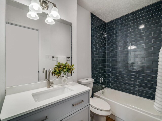 full bathroom with vanity, a textured ceiling, tiled shower / bath combo, and toilet