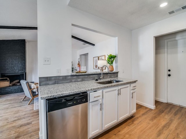 kitchen with light stone countertops, a fireplace, sink, dishwasher, and white cabinetry